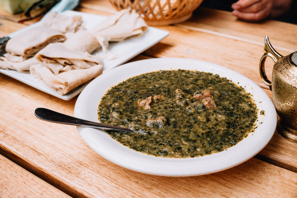 A green stew in a white bowl sits on a table next to a plate of Somalian bread. It's just some of the food to be tasted on a Foodie Trails tour of Melbourne