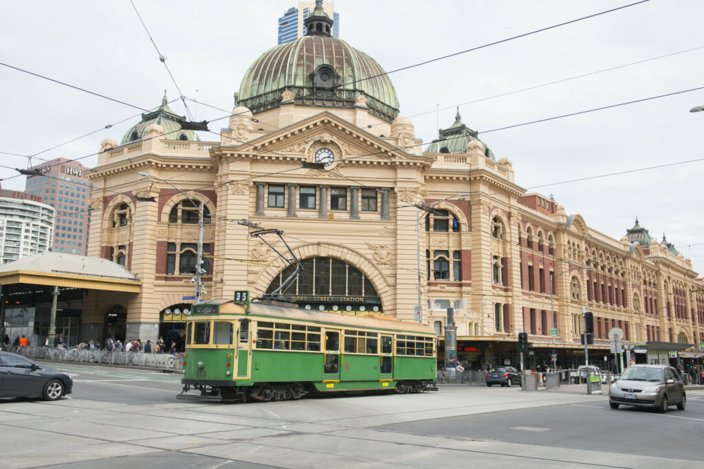 A green heritage tram passes in front of the iconic Flinders St Station in Melbourne