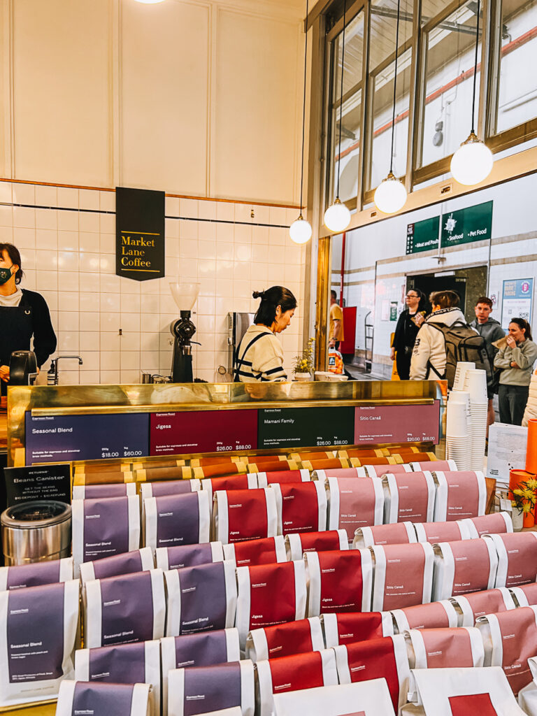 Interior of a coffee shop with a counter displaying various coffee blends in colourful packaging, with baristas and customers in the background.