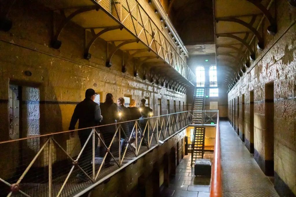 The inside of the haunted Old Melbourne Gaol shows five people walking along a metal gangway, each carrying lanterns.