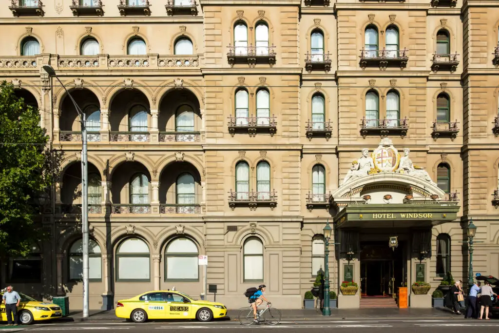 The exterior of the Hotel Windsor, with taxis waiting and a cyclist passing. The hotel is thought to be one of the most haunted places in Melbourne, with reports of ghost sightings.