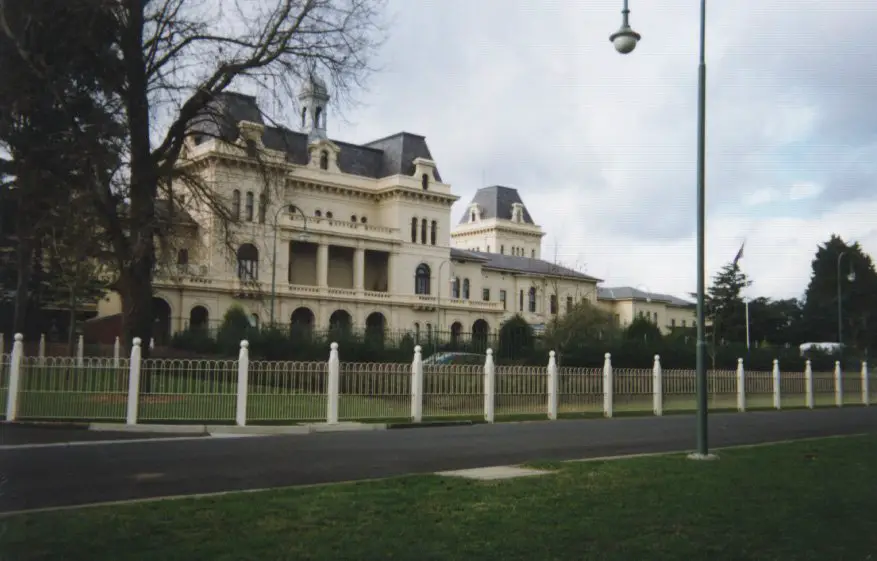 The exterior of Kew Asylum shows a large cream building with a grey roof. It has a white fence. This is believed to be one of the most haunted places in Melbourne.
