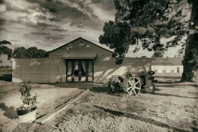 The exterior of Point Cook Homestead shows an old-fashioned home with an old tractor in front of it. The sky is filled with clouds.