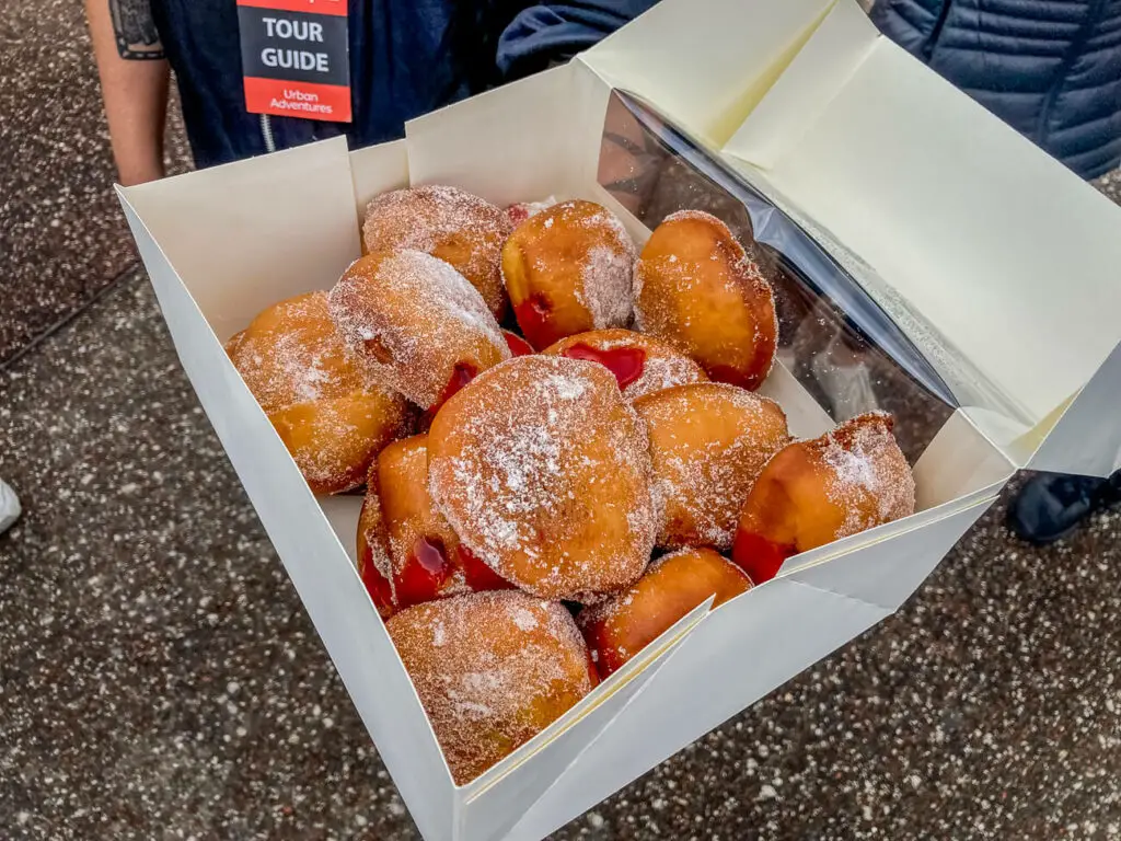 An overhead view of a white cardboard box filled with hot jam doughnuts, eaten on a walking tour in Melbourne, Australia. 