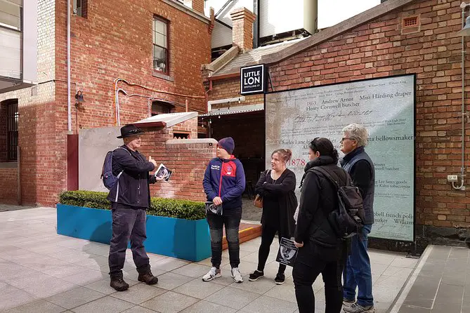 A man guides a group of people on a Melbourne Historical Walking Tour: Crime, Gangsters & Lolly Shops. The group stands in front of Little Lon Distilling Co, which was once an area that a lot of criminals visited